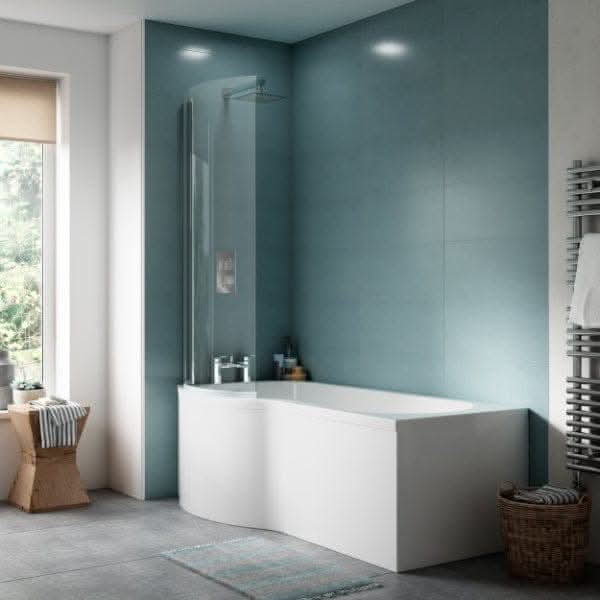 Modern bathroom with light blue wall tiles, a white curved bathtub fitted with the Nuie L Shaped Shower Bath Front Panel in white, glass shower screen, small window with beige shade, wooden stool, striped towel, and wall-mounted heated towel rail.