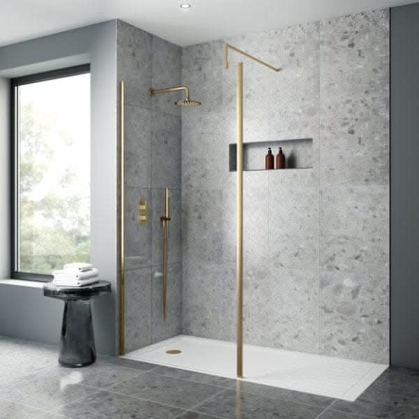 Modern bathroom with a walk-in shower featuring gold fixtures, Nuie Outer Framed Wetroom Screen with Support Bar, gray textured tiles, built-in shelf holding two bottles, window, and small black side table with folded white towels.