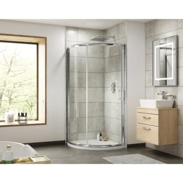 Modern bathroom with a Nuie Pacific Sliding Shower Door in chrome by Nuie, corner glass-enclosed shower, light wood vanity with vessel sink and mirror, large window, tiled walls, and a small gray rug on the floor.