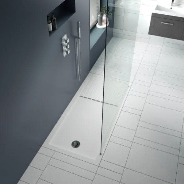 Modern bathroom with a Nuie Rectangular Walk-In Shower Tray, glass partition, wall-mounted controls, handheld showerhead, and grey tiled floor. Sink cabinet and mirror appear in the background.