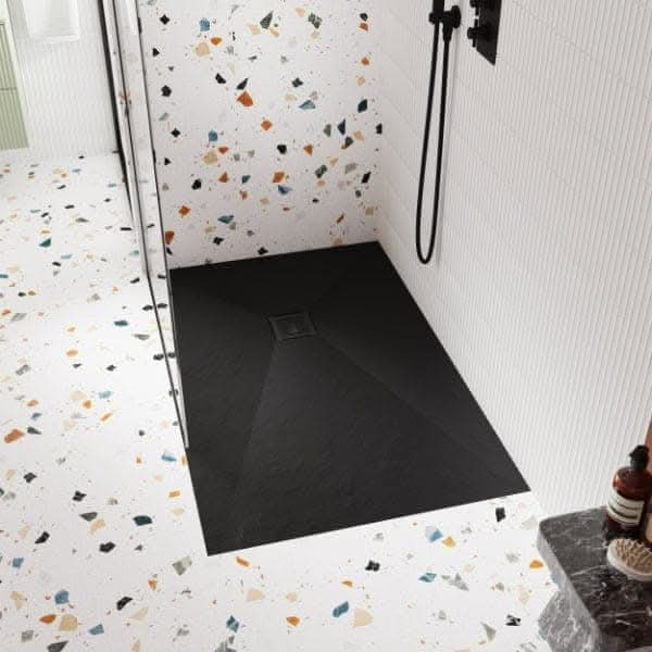 Modern bathroom with white, black, and colorful terrazzo tiles. Features a black rectangular shower base with the Nuie Square Shower Tray Waste by Nuie, a glass shower divider, black fixtures, and bottles and towel on a dark countertop.