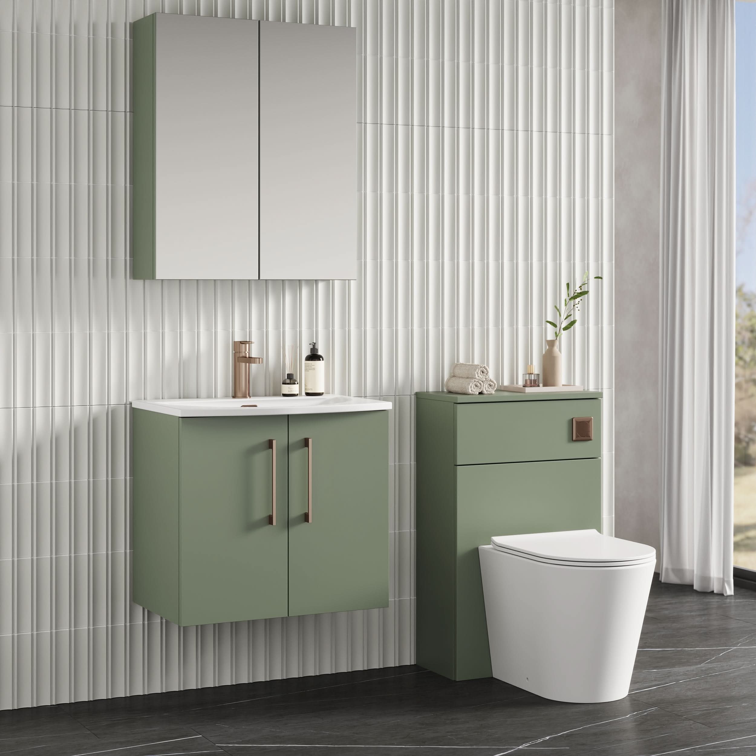 Modern bathroom with sage green Nuie Arno 2 Door Wall Hung Vanity Unit With Basin-4 (600mm), wall cabinet, white countertop sink, matching toilet unit, brass fixtures, decorative accessories, vertical white textured tiles, and right-side window light.