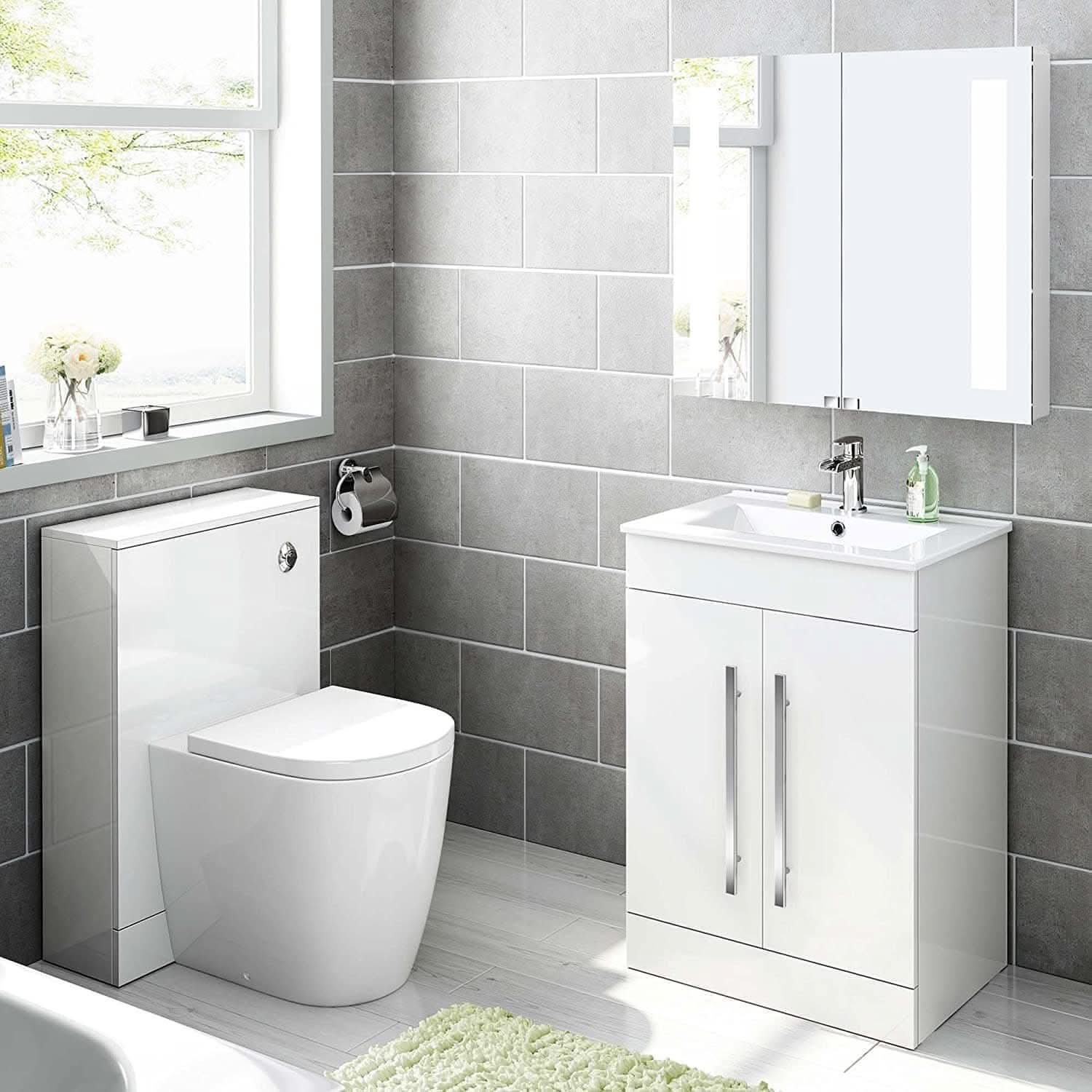 Modern bathroom with grey tiled walls, a white toilet with concealed cistern, and an iBathUK Avon 2 Door Floorstanding Vanity Unit With Basin (615mm x 815mm, 1 tap hole). Chrome handles, mirror cabinet, window light, and green bath mat complete the look.