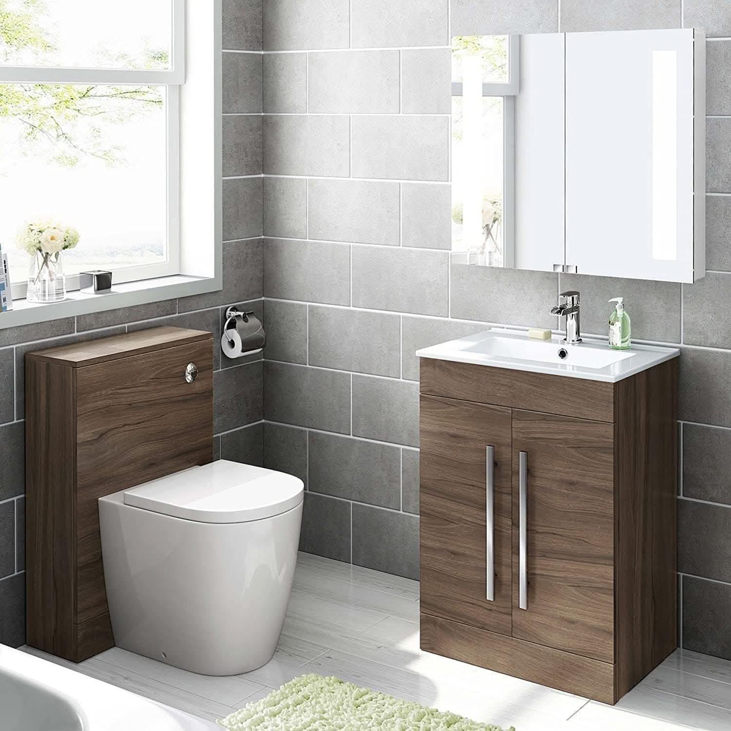 Modern bathroom with gray tiled walls, a window, white toilet with wooden unit, and an iBathUK Avon 2 Door Floorstanding Vanity Unit With Basin (615mm x 815mm, 1 Tap Hole). A mirror cabinet hangs above, with a soap dispenser and green rug on the white floor.