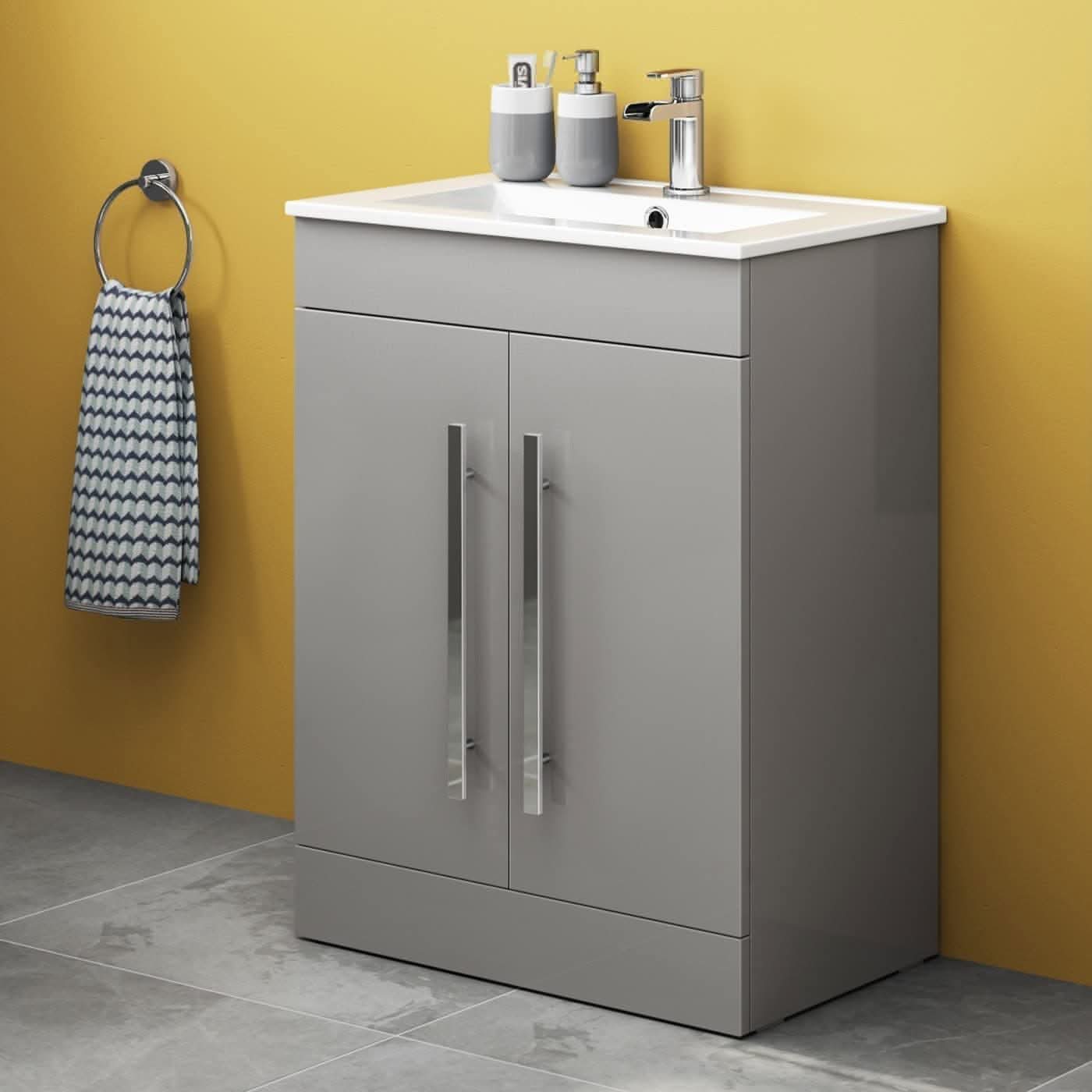 The iBathUK Avon 2 Door Floorstanding Vanity Unit With Basin (615mm x 815mm, 1 Tap Hole) features sleek silver handles, a white basin with a chrome faucet, and is styled with soap dispensers and a patterned towel on a yellow wall.