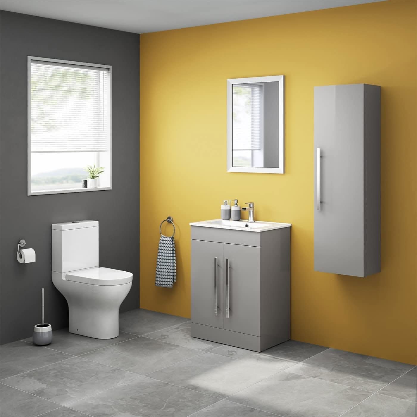 Modern bathroom with gray tile floor and yellow-gray walls, iBathUK Avon 2 Door Floorstanding Vanity Unit With Basin (615mm x 815mm, 1 tap hole), white toilet, tall gray cabinet, mirror, towel ring, toilet brush, blinds and potted plant.