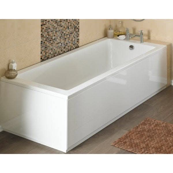 A modern white rectangular bath featuring the Nuie Straight Shower Bath End Panel With Plinth in gloss white and a chrome faucet, set against beige tiled walls with mosaic accents, with toiletries on the ledge and a brown bath mat on wooden flooring.
